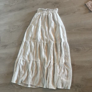 Vit långkjol från H&M med resår - Säljer en vit långkjol från H&M med bred smockresår i midjan. Kjolen har flera volanger och är gjord i ett lätt och luftigt bomullstyg, perfekt för varma dagar. Enkel att matcha med crop tops eller stickade tröjor för en chill look.