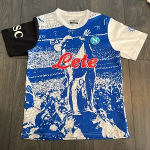 Napoli MARADONA fotbollströja ÖPPEN TILL BUD! - Napoli fotbollströja från EA7 i storlek Small. På tröjan är ett nästan lite ”Minecraft” aktikt motiv med en firande MARADONA på. Tröjan är mycket ovan att se på stan t.ex och man får mycket ”snygg tröja” när man använder den. Öppen till bud!🤗😊🙌