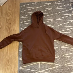 Brun hoodie från FB Sister i S - Säljer en brun hoodie från FB Sister i storlek S. Hoodien har en klassisk känguruficka framtill, huva och långa ärmar. Materialet är mjukt och känns som polyester, perfekt för höst och vinter. Enkel och stilren design utan mönster eller tryck.