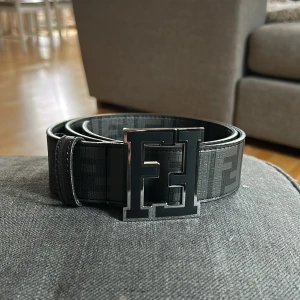 Fendi bälte - Sjukt snyggt Fendi bälte som är 105cm lång. Bältet har ett ikoniskt FF-mönster längs hela remmen och ett stort, metalliskt FF-spänne framtill. Bältet har en stilren, mörk design som verkligen sticker ut. Perfekt bälte för att lyfta din outfit. ALDRIG ANVÄND✅PRISET KAN DISKUTERAS!!