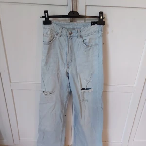 Ljusa wide jeans från H&M Divided - Säljer ett par ljusblå wide jeans från H&M Divided i storlek 38. Byxorna har hög midja, raka och vida ben samt slitna detaljer framtill.