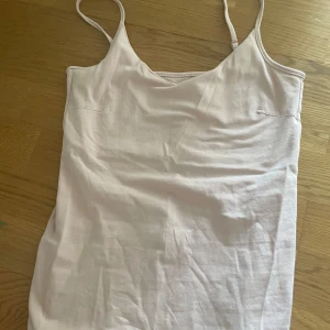 Ljusrosa linnetopp från 157 - Säljer en ljusrosa linnetopp från 157 med smala axelband och v-ringad hals. Toppen är i mjuk bomullsmix med lite stretch för extra komfort. Perfekt att styla med jeans eller kjol för en enkel och fräsch look.