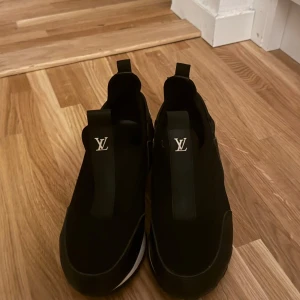 Svarta sneakers - Stilrena svarta sneakers med vit logga framtill och på hälen. Skorna har en sportig design med elastiska band och platt sula. Materialmix av textil och syntet ger en modern känsla. Perfekta för dig som gillar exklusiva streetwear-vibbar.