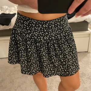 Svart blommig kjol med volang - Supersöt svart kortkjol med små vita blommor och volanger. Köpt på Gina Young för några år sedan. Superfin och i fint skick. Inga skavanker eller liknande!