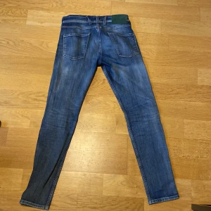 Blå Replay Anbass jeans slim fit - Säljer ett par blå Replay Anbass jeans i slim fit med klassisk femficksdesign. Jeansen har snygga slitningar och en mörkare tvätt, samt Replay-logga på fickan. Perfekta för dig som gillar en smalare passform och stilren look.   (Köpta för 1799kr)