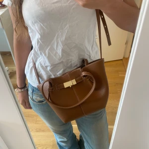 Brun axelväska i skinn med guldspänne - Säljer denna jätte trendiga och populära handväska från Lindex!! Nästintill slutsåld överallt, kan gå ner i pris vid snabb affär 🫰