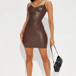Brun tight kort klänning i skinnimitation - Snygg brun kort klänning i skinnimitation med smala axelband och figurnära passform. Klänningen har v-ringad urringning och en minimalistisk look som ger en cool vibe. Perfekt för dig som vill sticka ut med en trendig och edgy stil.