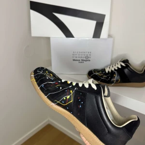 Maison Margiela Gats - Maison Margiela sneakers i svart med färgstänk, kvitto låda och skor får man med vid köp. Skorna är 9/10 sick och är enbart lite smutsiga och repade under sulan vilket är naturligtvis meningen pris går att förhandla och skorna säljs i befintligt sick. Se sista bilden för att se kvittot. Innesulan är bytt från orginal till extra sulorna man får med när man köper dem vilket sänker priset en del!