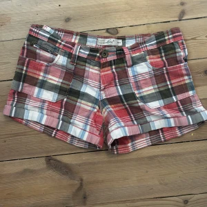 Rutiga shorts från Levi's - Färgglada rutiga shorts från Levi's i bomull. Shortsen har flera fickor fram och bak, och knappstängning. Mönstret går i rött, grönt, vitt och blått med inslag av beige och rosa. Perfekta för varma dagar och en chill stil. Färgerna är inte så starka i verkligheten, midjemåttet är ca 38 cm rakt över ❤️
