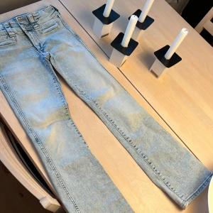Ljusblå bootcut jeans från H&M - Snygga ljusblå jeans från H&M med bootcut-ben och låg midja. Jeansen har justerbar midja och klassiska fickor fram. Perfekta för dig som gillar en avslappnad och trendig look. Materialet är mjukt denim i bomull.