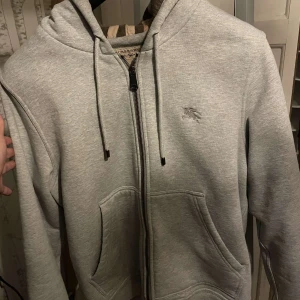Grå Burberry hoodie med dragkedja - Tja säljer min äkta burberry tröja i riktigt bra skick. Använd väldigt fåtal ggr då jag tycker den inte sitter så bra på mig. Hör av er vid funderingar