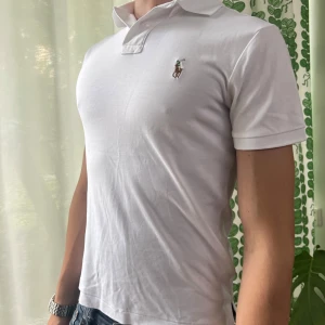 Vit polo t-shirt från Ralph Lauren XS - Vit polo t-shirt från Ralph Lauren i bomull, custom slim fit. Klassisk pikékrage, korta ärmar och broderad polospelare på bröstet. Perfekt för en clean och stilren look. Endast tröjan ingår.