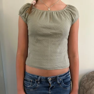 Ljusgrön croppad topp med kort ärm - Säljer en ljusgrön croppad topp med korta ärmar och lätt rynkad halsringning med små detaljer. Toppen har diskret hålmönster i tyget och är i mjuk bomull, perfekt till jeans eller kjol.