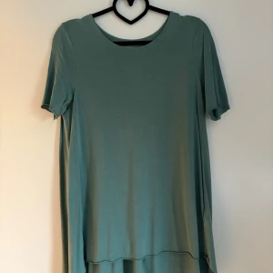 Grön topp från COS - Snygg grön topp från COS i 100% lyocell. Toppen har rund halsringning, korta ärmar och en alinjeformad, avslappnad passform. Perfekt för dig som gillar minimalistisk och stilren design.