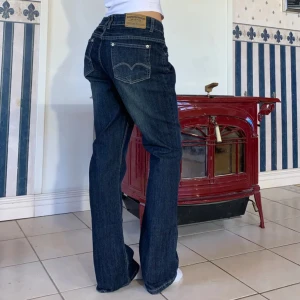 Levis 505 mörkblå jeans bootcut - Mörkblå Levis 505 jeans med klassisk femficksdesign och låg midja. Jeansen har raka ben med lätt bootcut och tydliga kontrastsömmar. Tillverkade i slitstarkt denim med snygg tvätt och Levis-logga på bakfickan.