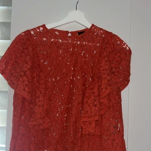 Röd spetsblus från Gina Tricot - Superfin röd blus från Gina Tricot i spets med blommigt mönster. Blusen har korta, vida ärmar och volangdetaljer på framsidan. Perfekt för dig som vill sticka ut med en färgstark och romantisk look.