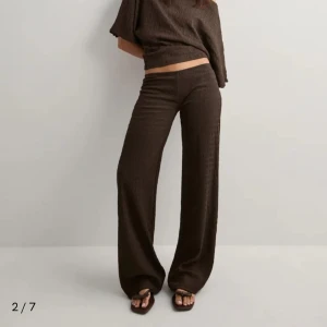 Brunt sett från Nelly  - Säljer ett sett där de är ett par bruna vida byxor från Nelly med snyggt ribbat tyg. Byxorna har låg midja och är tillverkade i ett mjukt, flowy material som ger en chill och trendig look. Toppen kan man ha på flera olika sett, of shoulder till exempel! 
