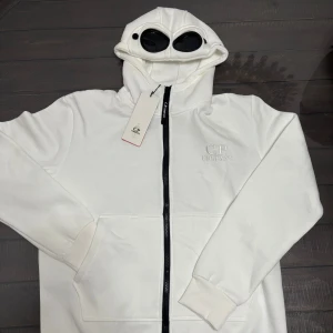C.P. Company hoodie - Säljer en clean vit hoodiejacka från C.P. Company med ikoniska goggles i huvan. Skriv gärna om du har funderingar, priset går att diskuteras