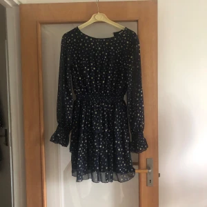 Marinblå klänning med stjärnor✨ - Supersöt mörkblå kortklänning med glittriga guldstjärnor, långärmad med volang vid ärmslut och resår i midjan. Tunt, flowigt material som ger en luftig känsla. Perfekt för dig som vill sticka ut med ett stjärnigt mönster och snygga detaljer.☀️