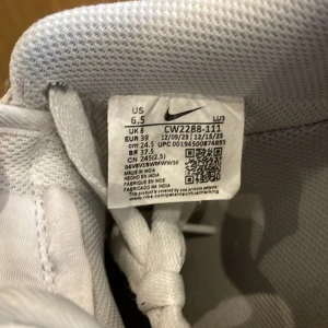 Nike Air Force 1 vita sneakers - Klassiska Nike Air Force 1 i helvitt skinn med lågt skaft och rund tå. Snygg och tidlös modell med perforerad tåbox, snörning och platt sula. Perfekta för dig som gillar en clean och sportig look. Har ett litet hål i vänstra skon