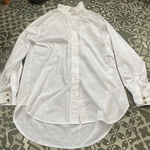 Vit oversized skjorta med knappar - Klassisk vit skjorta i bomull med lång ärm, bröstficka och knappar framtill. Skjortan har en oversized passform och rundad nederkant! ☀️