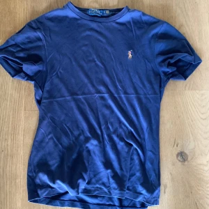 Marinblå t-shirt Polo Ralph Lauren - Snygg marinblå t-shirt från Polo Ralph Lauren i slim fit-modell. Klassisk design med korta ärmar och rund hals. Ikoniska broderade polospelaren på bröstet. Tillverkad i mjuk bomull som känns skön mot huden.