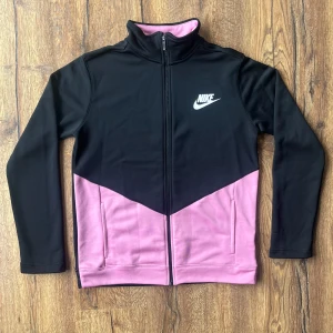 Nike zipjacka svart och rosa XL/158-170 - Nike jacka i svart och rosa med hel dragkedja och hög krage, Nike märke på bröstet och två fickor framtill. Aldrig använd! 🩷🖤