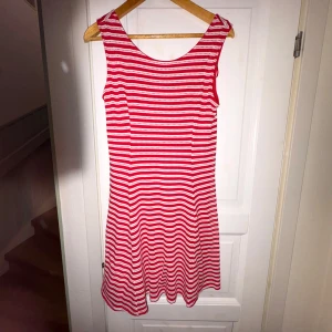 Rödvit randig ärmlös klänning - Snygg ärmlös klänning från Bondelid  med röda och vita horisontella ränder. Fantastisk kvalitet! Modellen är kort och har en rund halsringning. Perfekt för varma dagar och enkel att styla med sneakers eller sandaler.