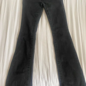 True Religion svarta bootcut jeans - Svarta jeans från True Religion, modell Becca Mid Rise Bootcut. Populära jeans så passa på! Har Snygga fickor med lock och logoknappar bak, klassisk bootcut passform och normal midja. Jeansen är i stretchigt denim och har coola detaljer som ger en edgy vibe. 