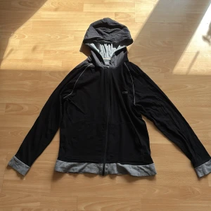 Svart hoodiejacka från BOSS, M - Svart hoodiejacka från BOSS med gråa muddar och huva. Jackan har dragkedja framtill, gråa detaljer längs ärmarna och en avslappnad passform. Perfekt för chill dagar eller när du vill ha en clean streetstyle-look och speciellt för dig som gillar tunnare kläder. Jag säljer koftan för att jag inte gillar att den är tunn och den ligger bara i garderoben.
