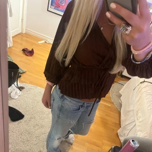 Jättesnygg blus i från Zara - Säljer en snygg plisserad brun omlottblus från Zara med knyt i midjan och v-ringad hals. Blusen har långa ärmar med resår vid ärmslut och ett glansigt material som ger en cool look. Perfekt att styla med jeans eller kjol för en trendig vibe.