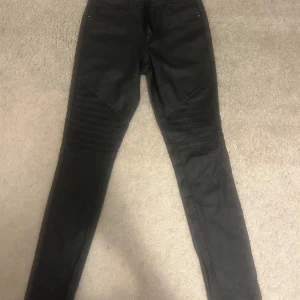 Svarta skinny jeans från ONLY - Svarta skinny, läderbyxor från ONLY med coola ribbade detaljer över knäna. Byxorna har klassisk femficksdesign och är tillverkade i stretchigt material för en tight passform. Perfekta för dig som gillar en edgy och modern look.