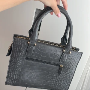 Grä väska med guld detaljer  - En jättefin grå handväska med guld detaljer och ett långt väsk band. Från Don Donna