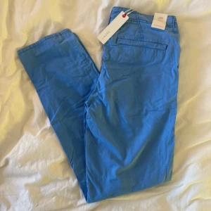 Blå chinos slim fit från Esprit - Snygga blå chinos från Esprit i slim fit-modell med medelhög midja. Byxorna har klassiska fickor fram och bak, bälteshällor och stängs med knapp och dragkedja. Perfekta för dig som gillar en stilren och fräsch look.