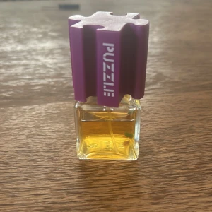 PUZZLE parfym 50 ml med lila lock - Unik parfymflaska från Pierre Robert med coolt lila lock i form av en pusselbit och transparent glasflaska. Innehåller 50 ml gyllengul vätska. Perfekt för dig som gillar annorlunda och lekfull design på din parfym. Pussel inne i parfymen med😁 Köpt sacond hand för 800 då den var riktig cool och doften sitter kvar så länge minst 2 dygn typ. Kan inte så mycket om denna doft tror den är från 90'