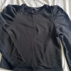Svart långärmad tröja från Zara - Svart långärmad tröja från Zara i mjuk bomull. Tröjan har puffade axlar som ger en trendig siluett och rund halsringning. Perfekt att styla med jeans eller kjol för en clean look.