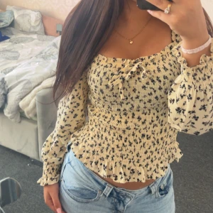 Blommig blus från FP Sister XS - Supersöt blommig blus från FP Sister i beige med svarta små blommor. Smockad överdel, volangkant nertill och långa puffärmar med resår vid handlederna. Snygg knytning framtill och fyrkantig ringning💞