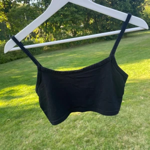 Svart croppad linnetopp från HM - Enkel och stilren svart croppad linnetopp från HM med smala axelband. Perfekt att matcha med höga jeans eller kjol. Mjuk och skön bomullskänsla, passar dig som gillar minimalistisk stil.