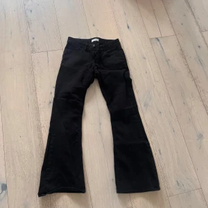 Svarta bootcut jeans från Lindex - Svarta jeans från Lindex i klassisk bootcut-modell. Byxorna har fem fickor, bälteshällor och dragkedja med knapp. Snygg passform och tillverkade i ett mjukt bomullstyg med lite stretch för extra komfort.