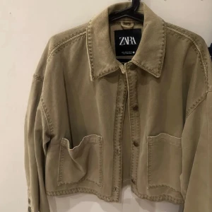 Beige overshirt från Zara - Snygg beige overshirt från Zara med stora fickor framtill och klassisk krage. Jackan har en croppad passform och knappar längs framsidan. Perfekt att slänga över en hoodie eller t-shirt för en chill look.