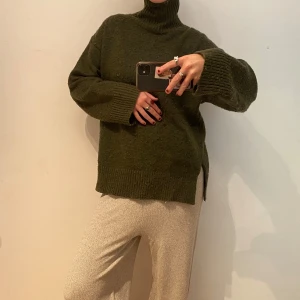 Olivgrön polotröja i ull - Säljer en olivgrön polotröja med oversized passform och långa ärmar. Tröjan är stickad i mjuk ull och har breda ribbade muddar vid ärmslut och nederkant samt hög polokrage. Perfekt för kalla dagar och chill outfits.