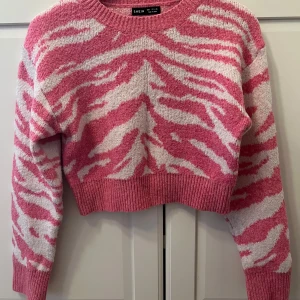 Rosa och vit croppad stickad tröja SHEIN - Säljer en croppad stickad tröja från SHEIN i storlek S. Tröjan har ett coolt zebramönster i rosa och vitt, rund hals och långa ärmar.