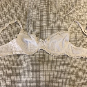 Vit spetsig bygel-bh B75 - Söt vit bygel-bh med tunna axelband och spetskant runt kuporna. Bh:n har diskret ribbat mönster och små håldetaljer i tyget, samt en liten rosett framtill. Endast provad.