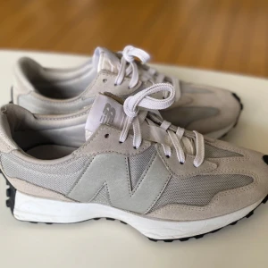  New Balance sneakers, grå,  i mocka Stl 41,5 - Snygga sneakers från New Balance (327)  i ljusgrå och beige toner. Ovandel i mocka och mesh med stora N-loggor på sidorna. Vita snören och vit mellansula, samt svart yttersula med  gummidetaljer. 
