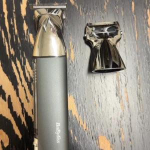 BaByliss hårtrimmer i metallgrå - BaByliss hårtrimmer i metallgrå med kromade detaljer och utbytbart rakhuvud. Ergonomisk design med slimmad form och robust metallkropp. Perfekt för att fixa skarpa linjer och detaljerade frisyrer. Laddningsbar och enkel att använda.