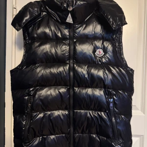 Moncler dunväst svart stl 3 (M–S) - Äkta Moncler dunväst i svart, storlek 3 – passar M eller liten S. Klassisk modell med hög krage, två dragkedjefickor och ikonisk Moncler-logga på bröstet. Lätt, varm och perfekt för lager på lager under höst och vinter. Helt ny, oanvänd  📍 Finns i Stockholm kan skickas mot frakt 💸 Pris: 2000 (kan gå ner) 