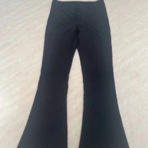 Svarta bootcut byxor Gina Tricot M - Svarta bootcut byxor från Gina Tricot i storlek M. Byxorna har klassisk passform med utsvängda ben och knäppning fram. Snygga bakfickor med knappdetalj. Perfekta för dig som gillar en stilren och trendig look.