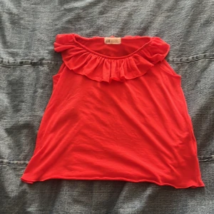 Röd volangärmlös topp från H&M - Superfin röd topp från H&M med bred volang runt halsringningen. Ärmlös modell i mjuk bomull, perfekt för varma dagar. Snygg och enkel att matcha med jeans eller kjol för en färgstark look.