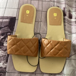 Beige quiltade sandaler från G - Stilrena sandaler i beige med bred quiltad rem i syntetmaterial. Fyrkantig tå och platt sula ger en modern vibe. Perfekta för varma dagar när du vill ha en clean look.