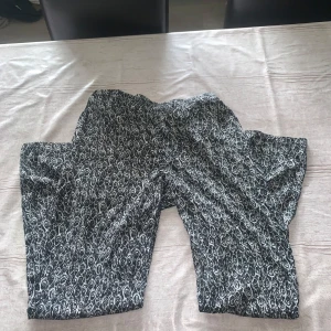 Svarta mönstrade byxor med vitt - Snygga svarta byxor med vitt mönster som ger en cool och unik vibe. Byxorna har rak passform och är perfekta för dig som gillar att sticka ut. Materialet känns mjukt och skönt mot huden, och mönstret är riktigt detaljerat. Passar till både sneakers och boots.